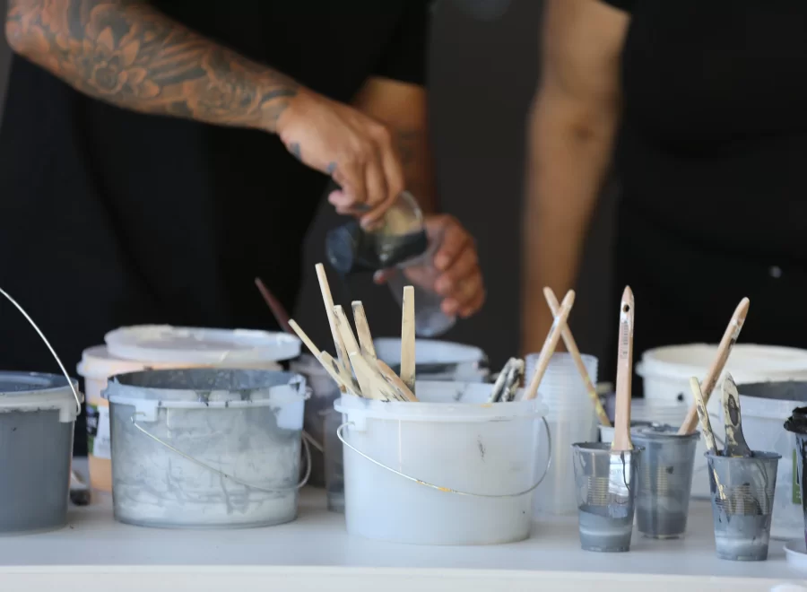 Paint pots in various shades of white and grey sit on a table with paintbrushes sticking out of them