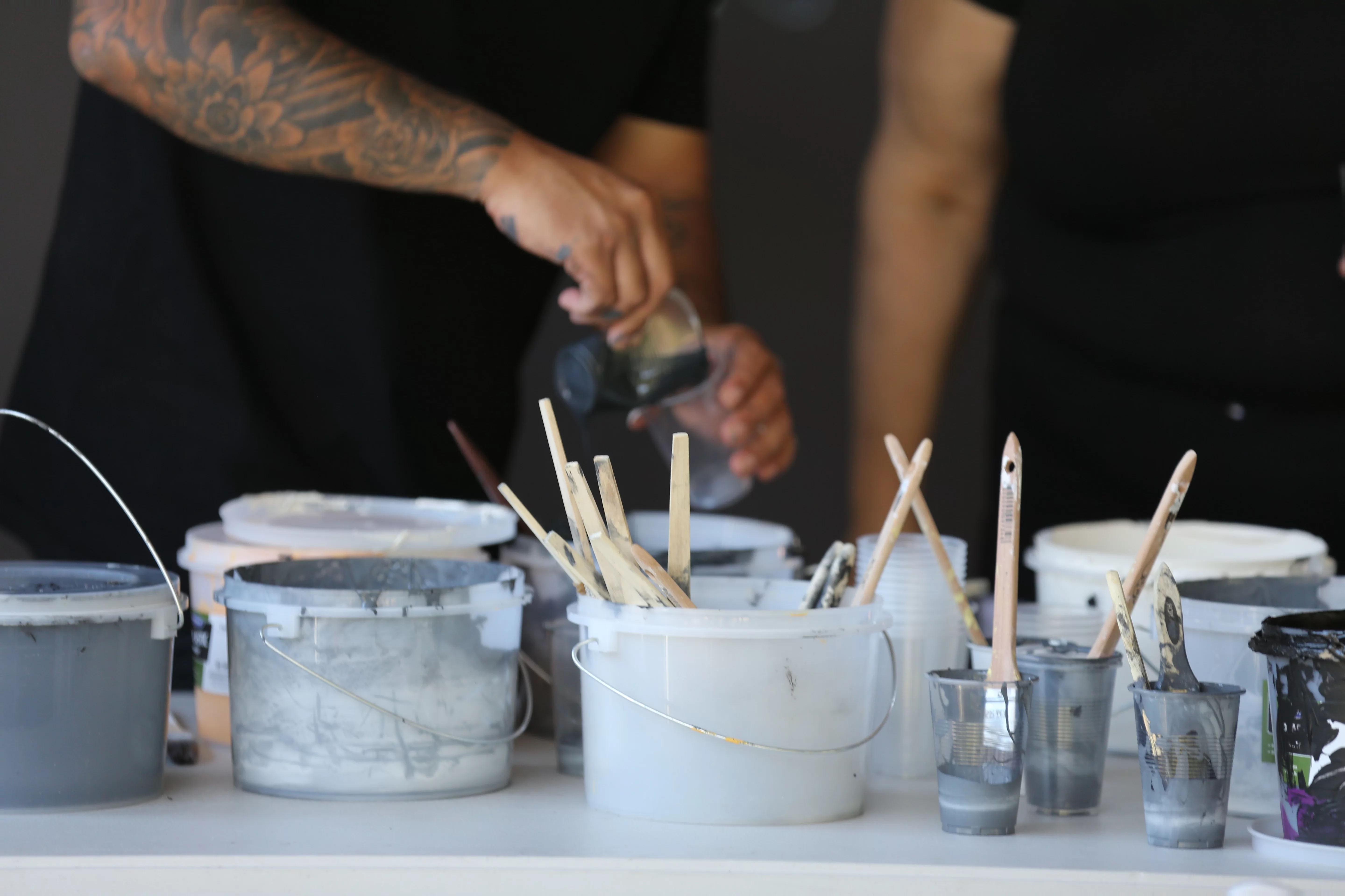 Paint pots in various shades of white and grey sit on a table with paintbrushes sticking out of them